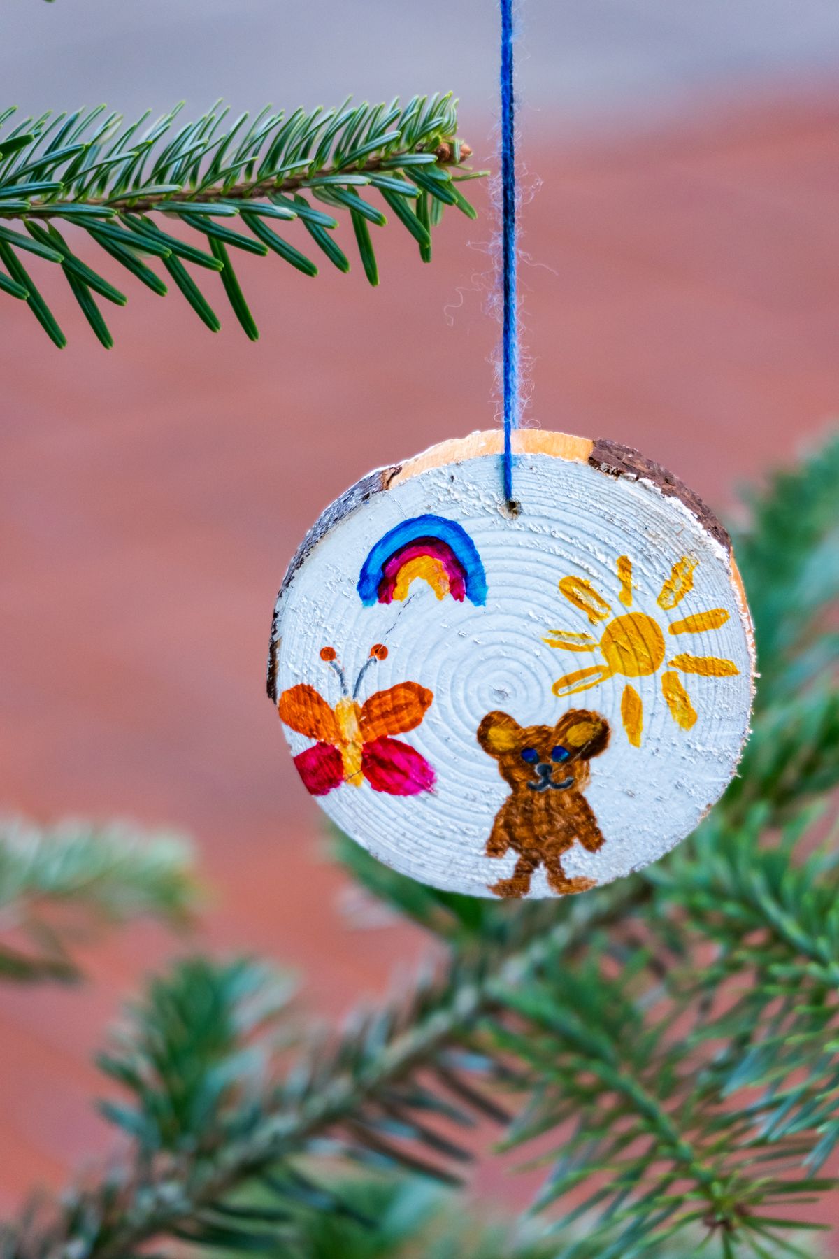 Wood slice craft ideas with a painted wood slice ornament with twine hanging on a branch