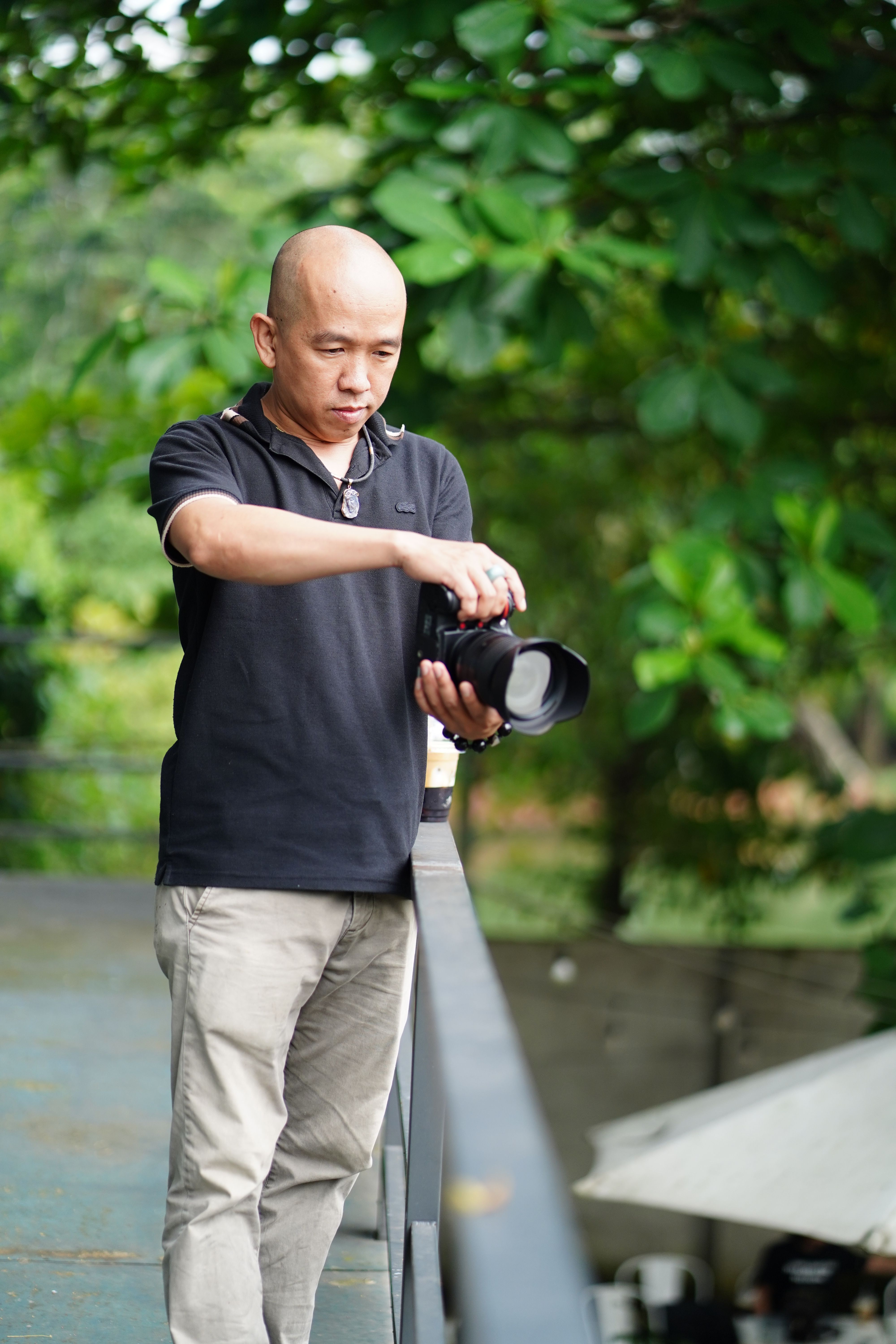 A photographer prepares his camera on a railing in a lush outdoor setting.