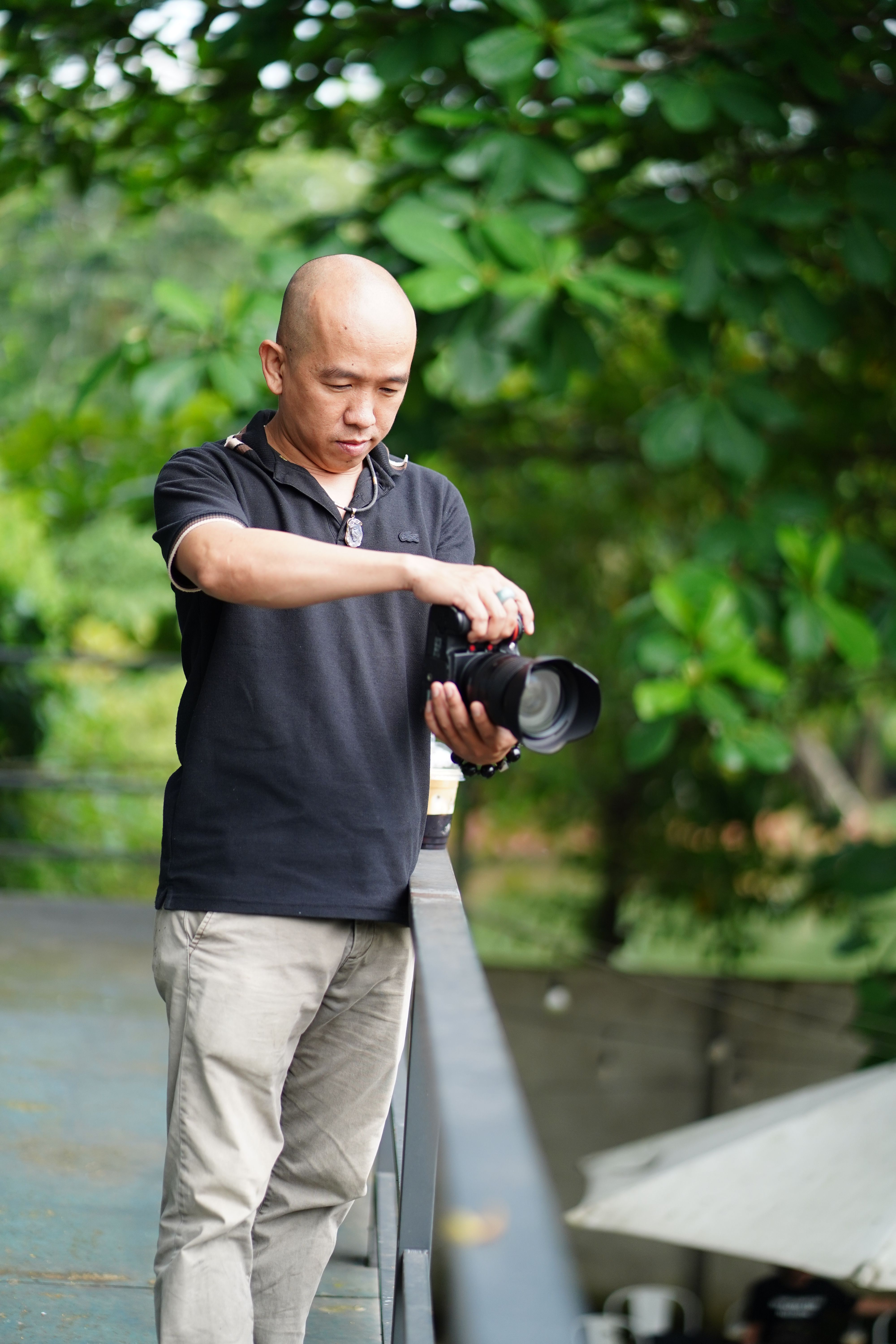 A man adjusting his camera, surrounded by lush greenery, during the day.
