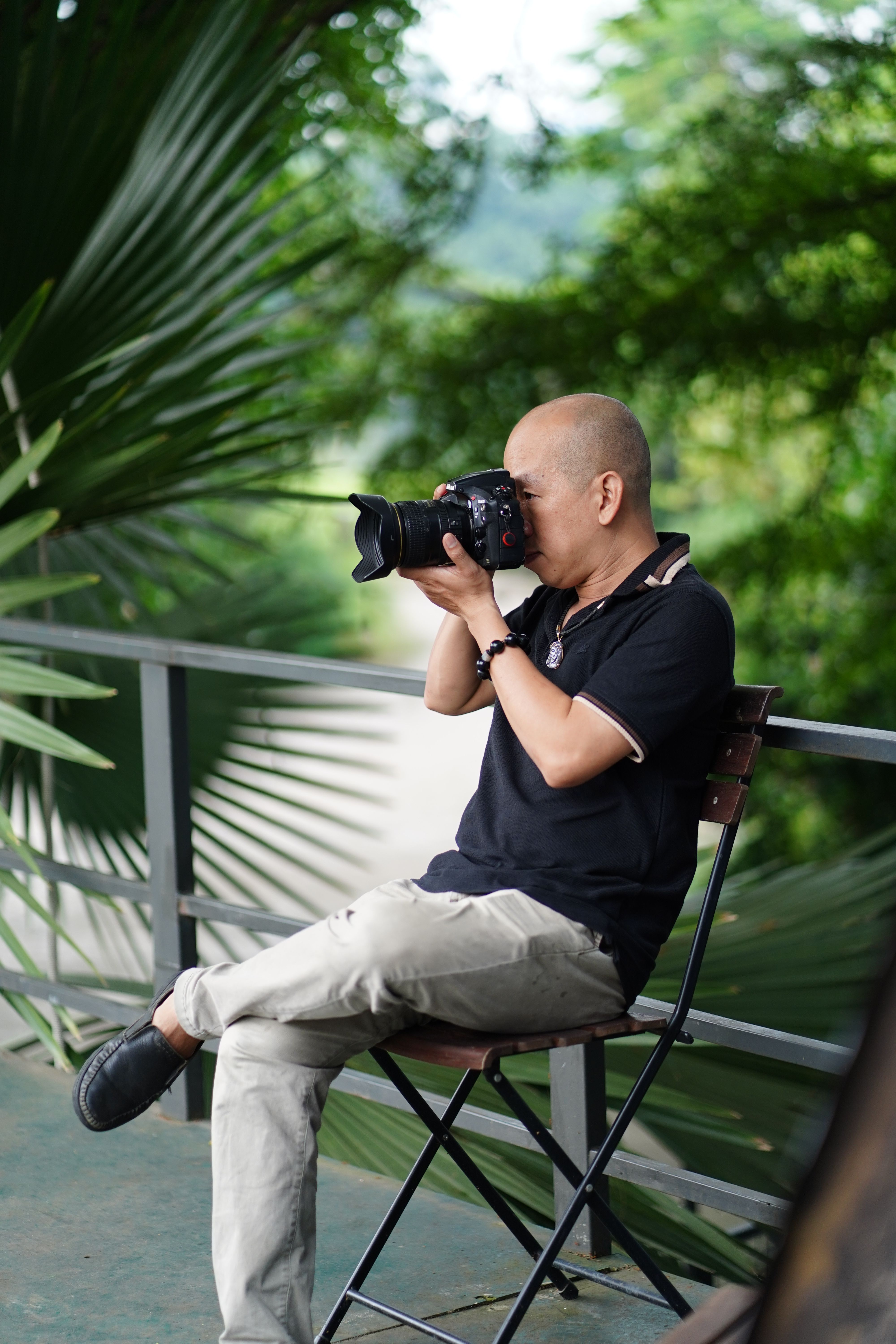 A photographer taking pictures outdoors, surrounded by lush greenery and palm leaves.