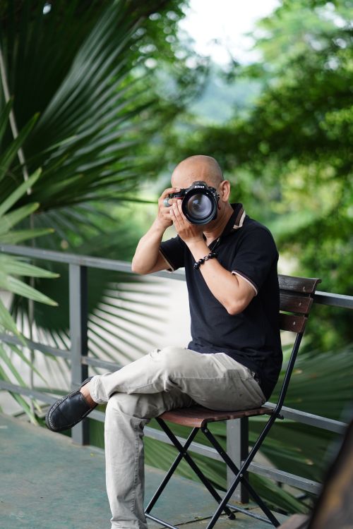 Free Adult photographer taking pictures in lush green outdoor setting, seated on chair. Stock Photo