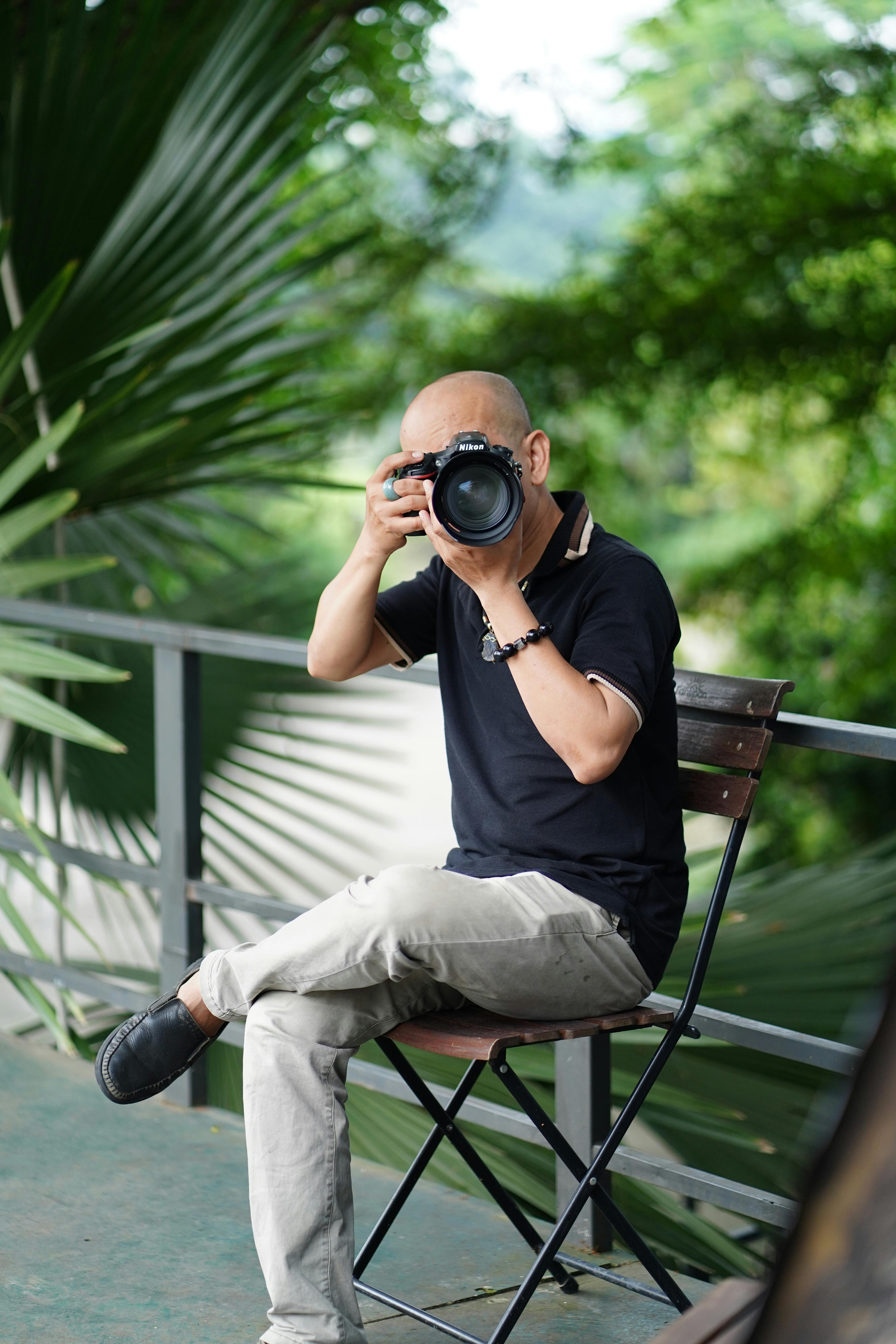 Free A skilled photographer sitting outdoors capturing nature with a DSLR camera. Stock Photo