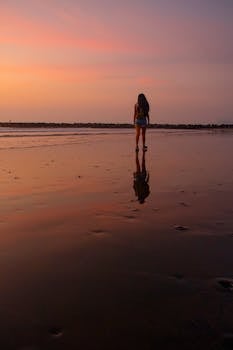 A serene sunset view on Trujillo beach, Peru, with a woman walking on the shore. Reflective and calming scene.