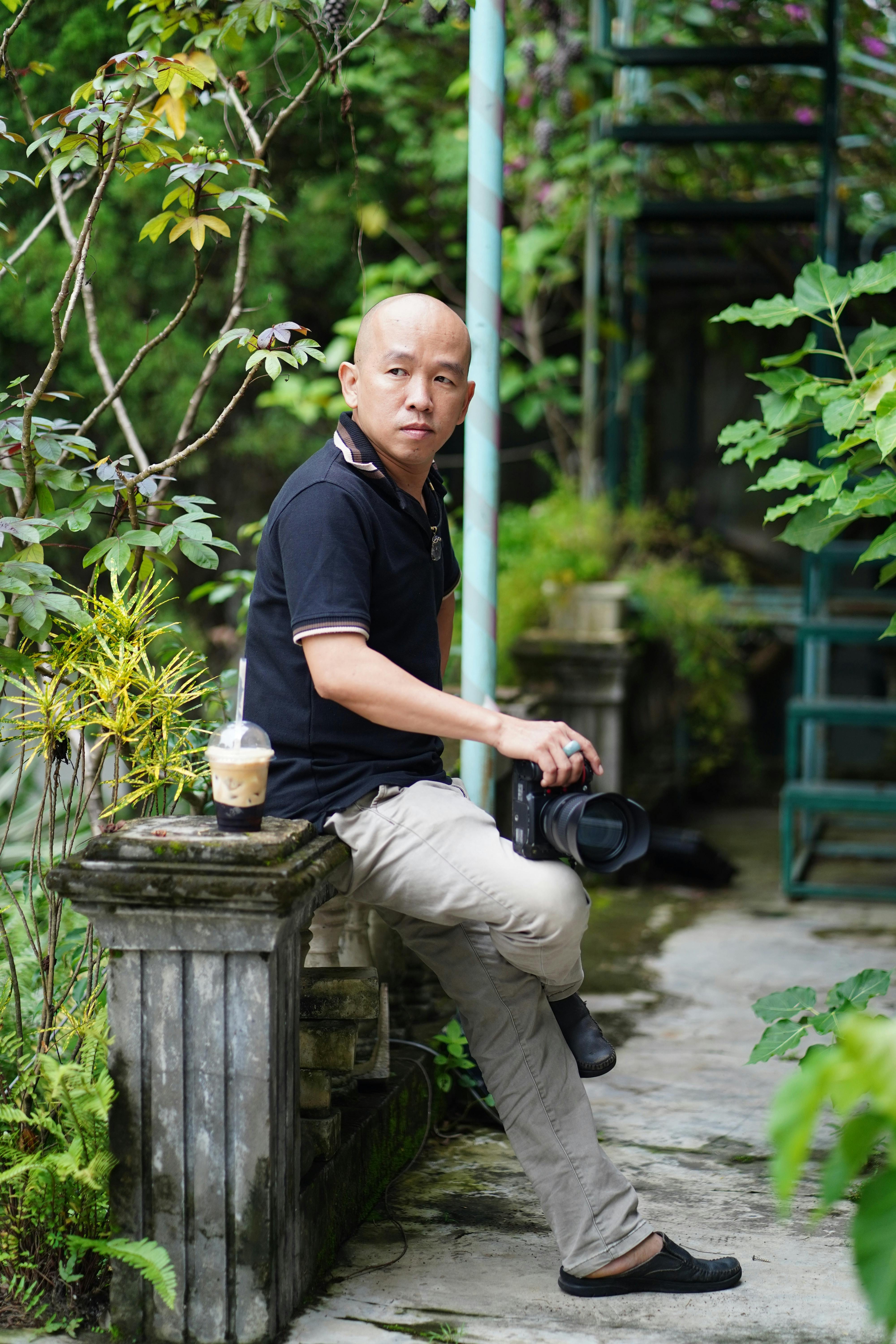 Man sitting with camera in a lush outdoor garden setting, enjoying a coffee.