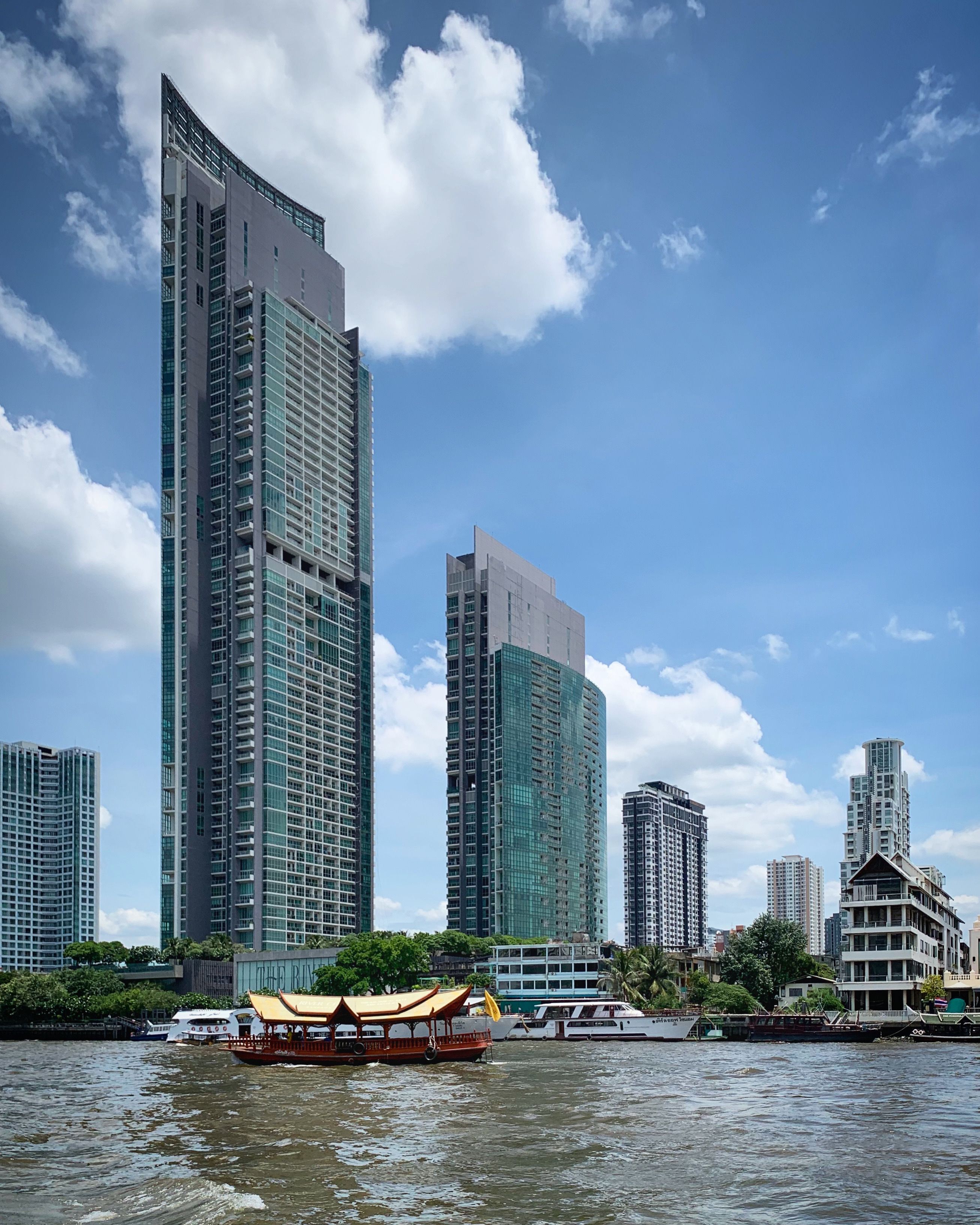 Stunning view of Bangkok's modern skyline with skyscrapers along the Chao Phraya River, featuring traditional boats.