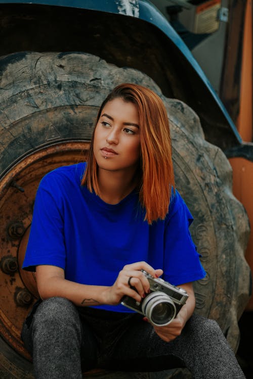 Woman Holding Camera Sitting at Vehicle Tire