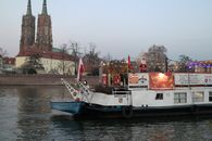 A Christmas-themed boat on the Odra River in Wrocław with the Cathedral of St. John in the background.