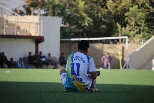 A young soccer player sitting and observing a game during a sunny day in Quetta.
