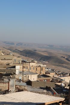 Scenic view of a rustic village with stone houses overlooking arid hills under a clear sky.
