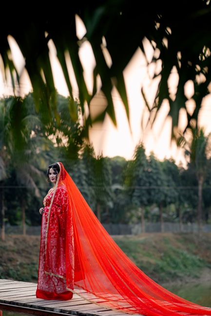 A South Asian bride in traditional red attire and long veil in an outdoor setting, capturing wedding elegance.