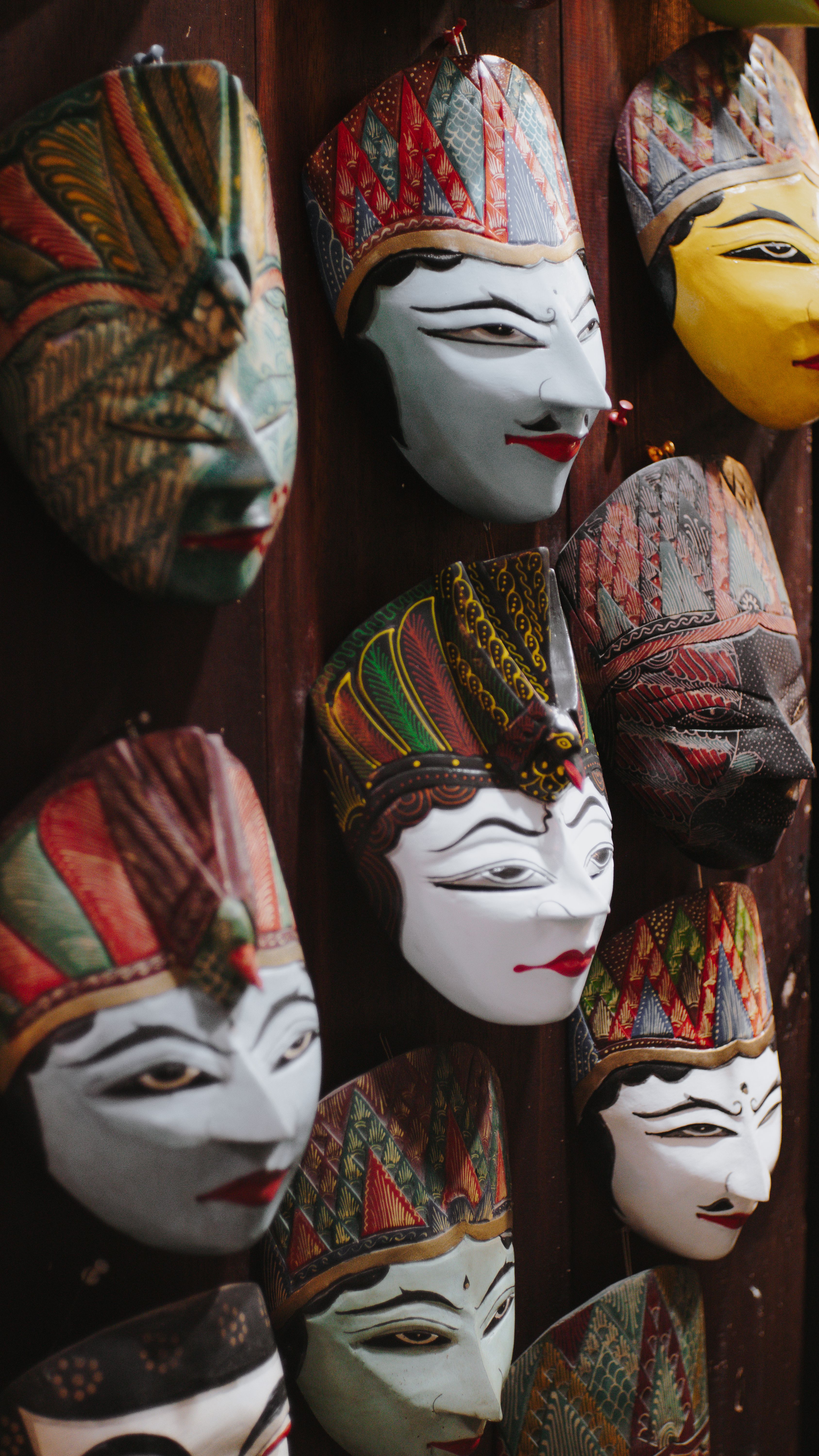 A collection of colorful traditional masks displayed on a wooden wall, showcasing intricate designs.