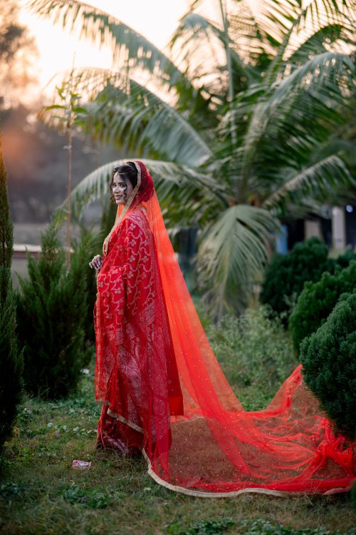 Free A South Asian bride stands gracefully in a vibrant red sari outdoors. Stock Photo