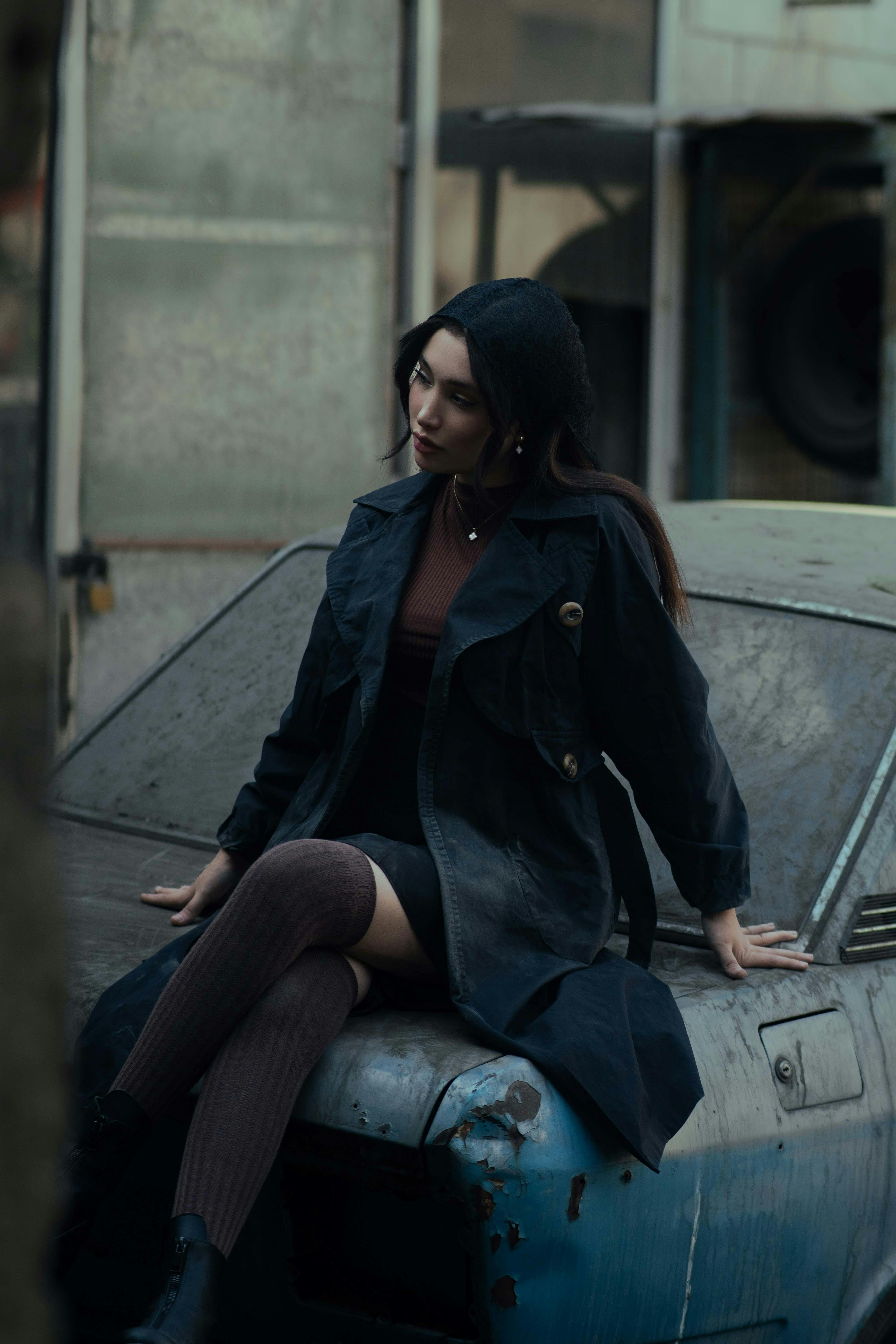 Portrait of a fashionable woman sitting on an old car, urban Tehran background, moody tone.