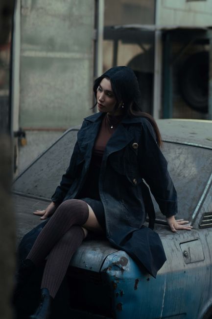 Portrait of a fashionable woman sitting on an old car, urban Tehran background, moody tone.