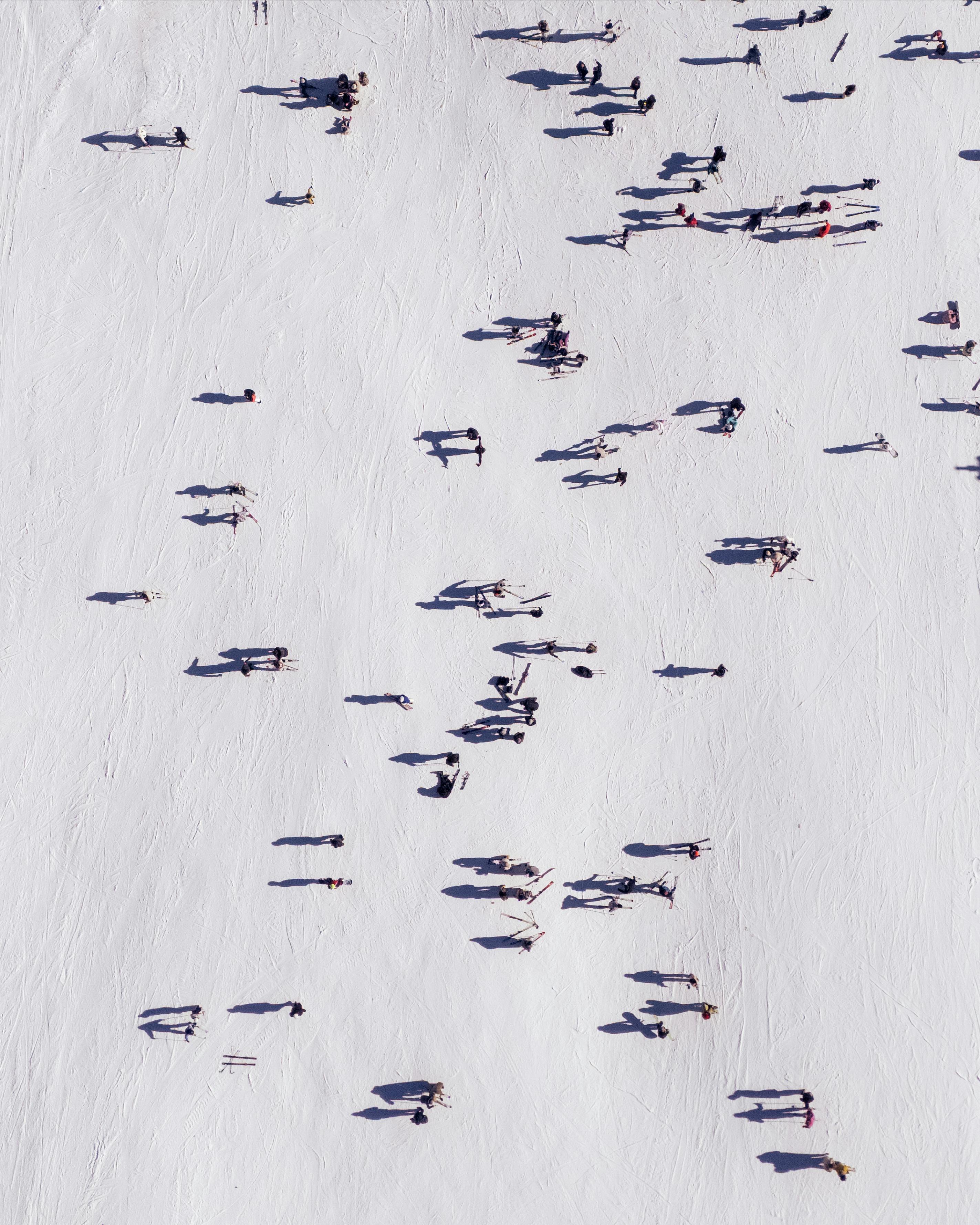 Aerial perspective capturing skiers casting long shadows on a snow-covered slope, illustrating dynamic winter activity.