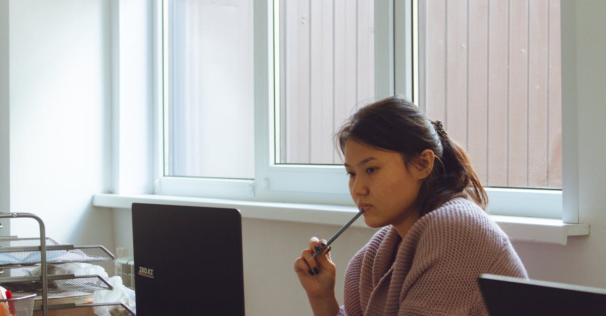 Photo by Kenzhar Sharap Young woman in cozy sweater working intently on laptop at desk.