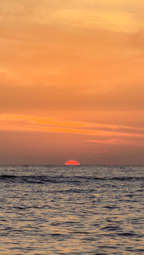 Free Captivating sunset over the ocean with a striking orange sky, creating a serene and peaceful atmosphere. Stock Photo