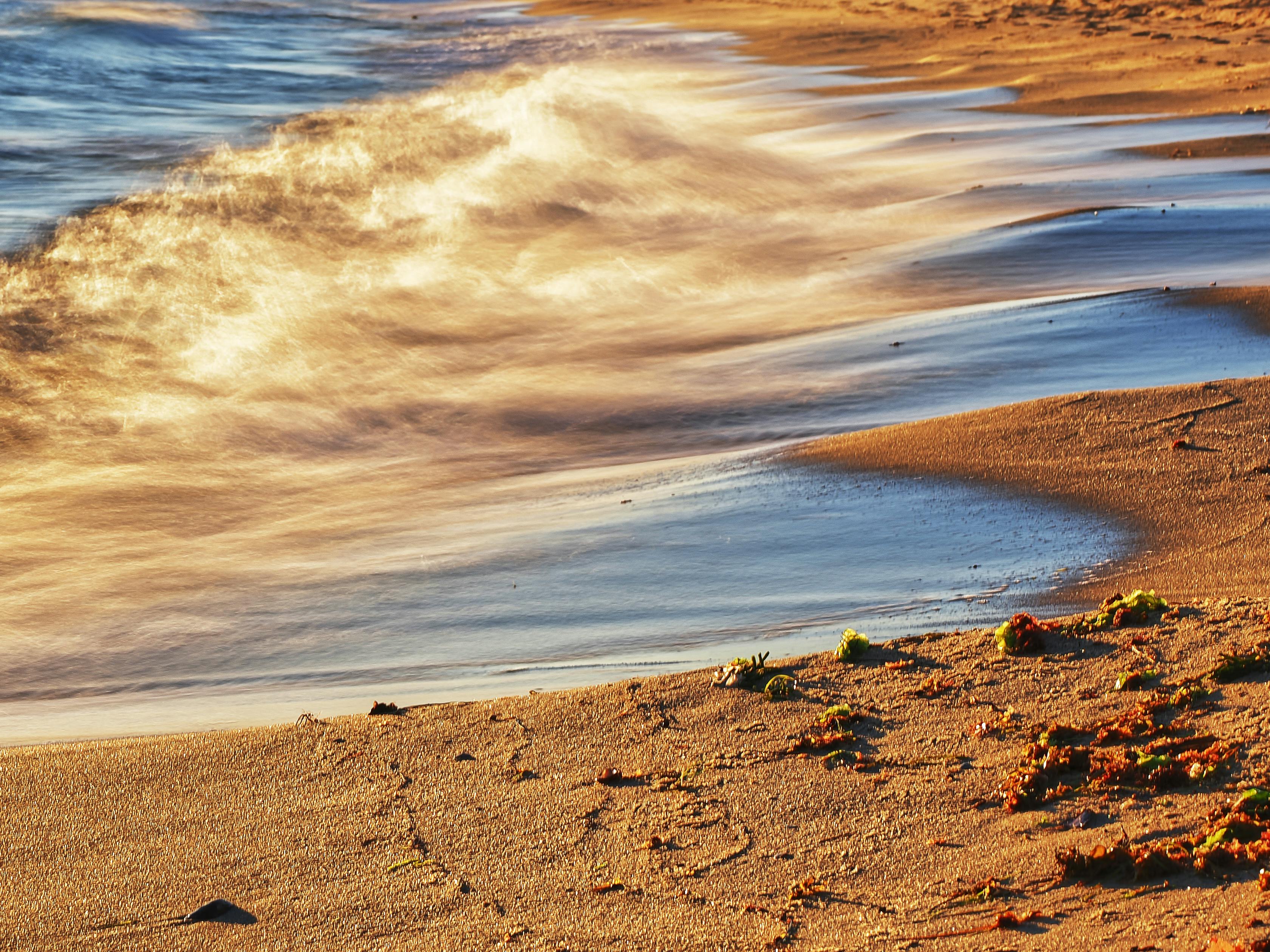 Una escena de playa serena capturando olas doradas bajo el sol poniente, creando una atmósfera costera pacífica.