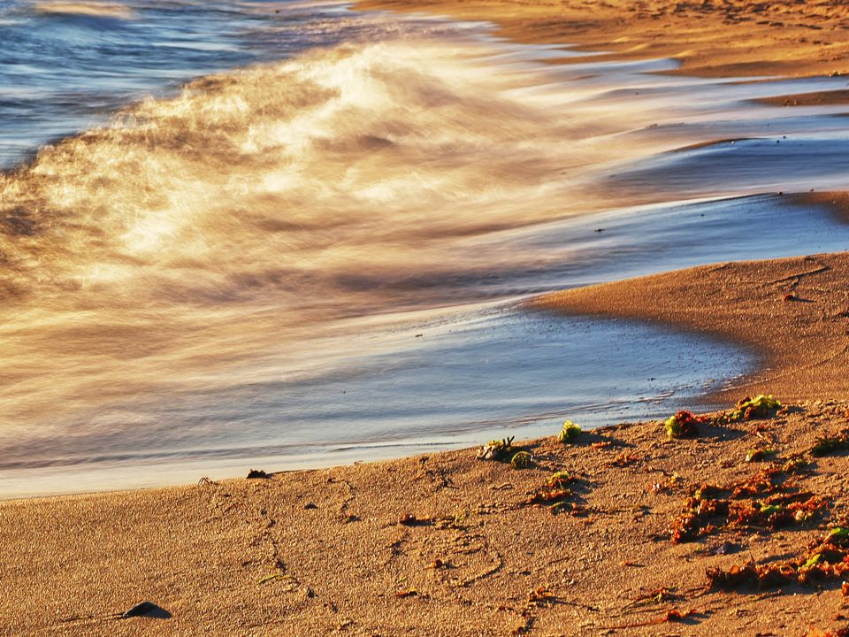 A serene beach scene capturing golden waves under the setting sun, creating a peaceful coastal atmosphere.