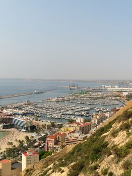 Aerial view of Alicante's marina with boats, coastline, and cityscape under a clear sky.