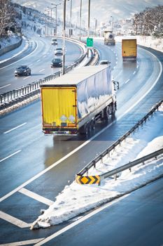 Highway scene with trucks and cars driving on a snowy winter day.