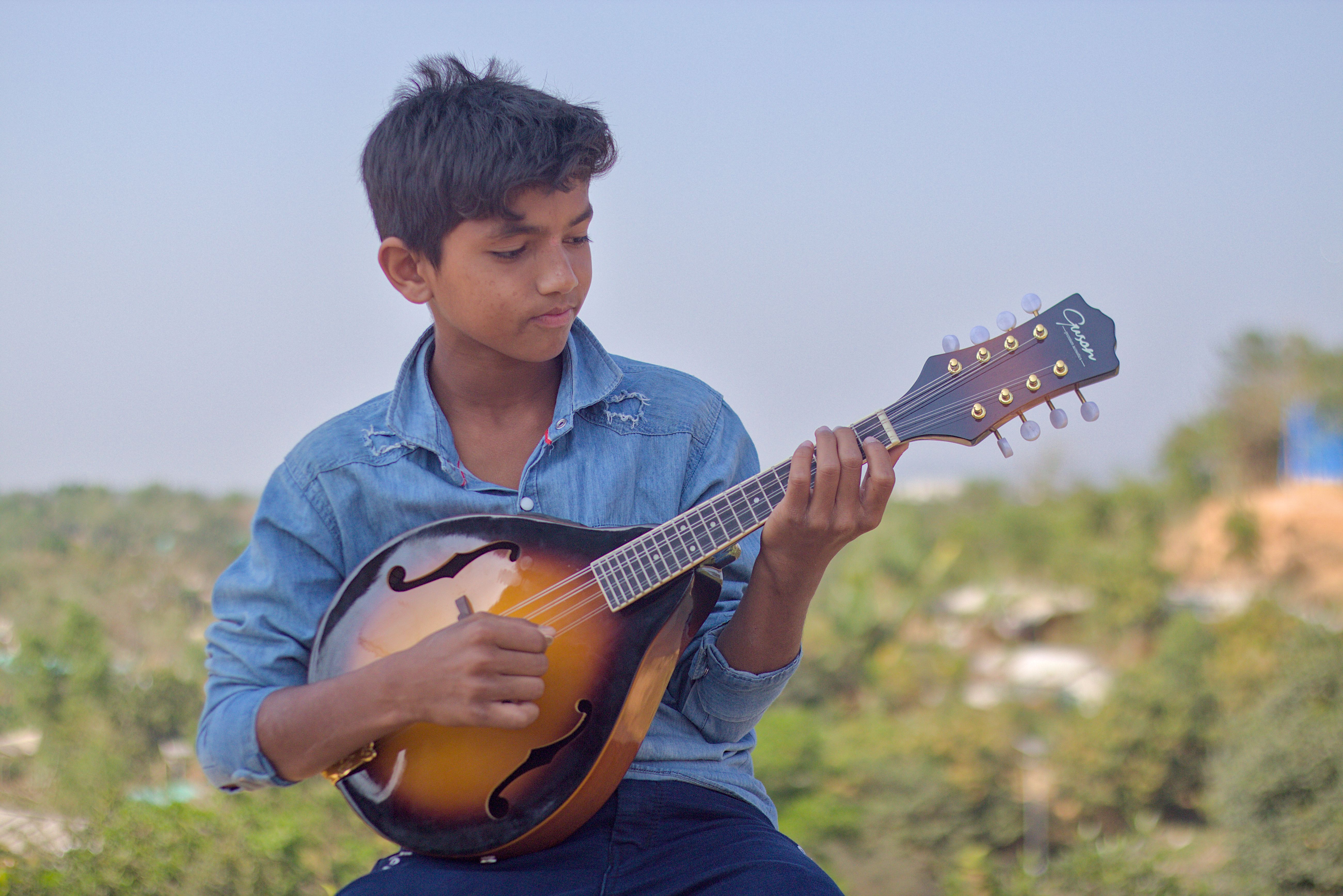 Rohingya teenager playing a mandolin in an outdoor setting, expressing cultural music.