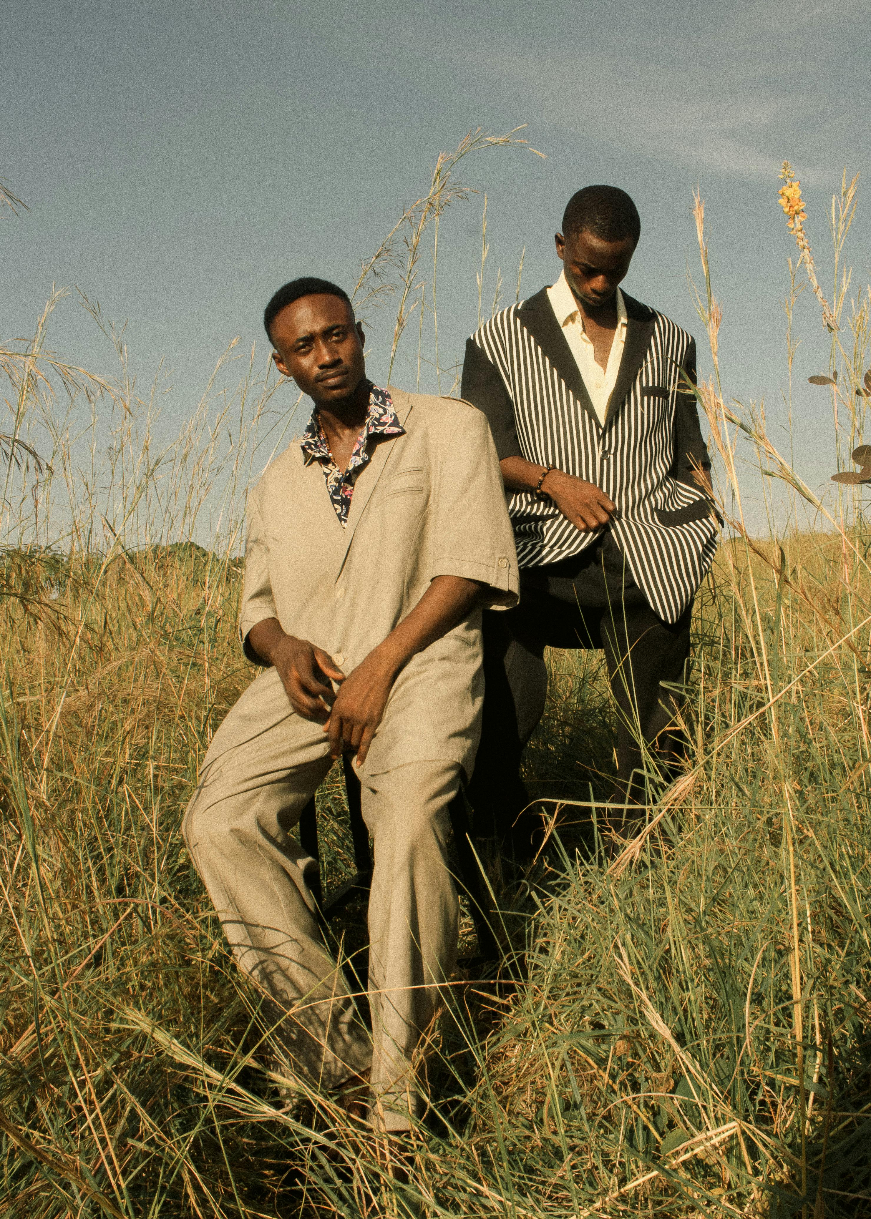 Zadarmo Dvaja muži v štýlových oblekoch pózujú na slnkom zaliatej trávnatej lúke a predvádzajú módu. Fotka z fotobanky