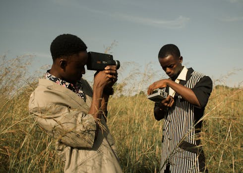 Two men with vintage cameras amidst tall grass showcasing a unique fashion shoot.