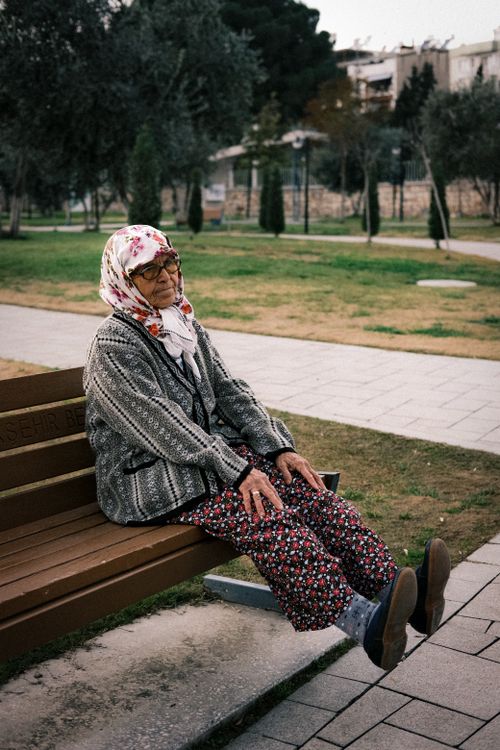 Free Elderly woman wearing a headscarf sitting on a park bench, deep in thought, on a peaceful day. Stock Photo