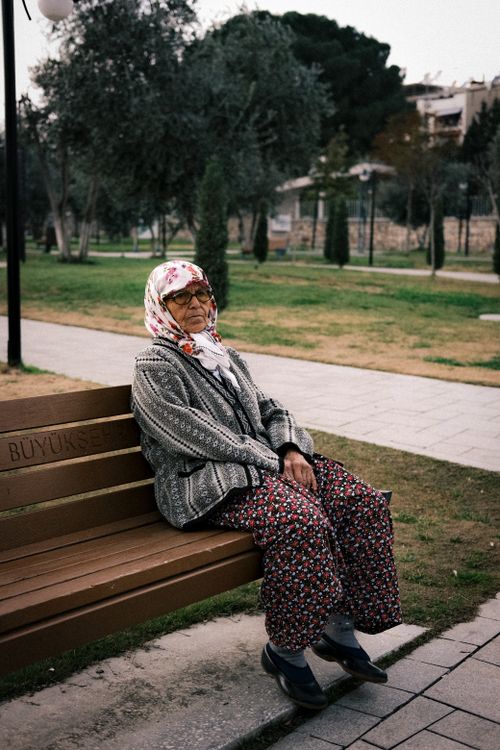 Free An elderly woman in floral attire sits on a park bench enjoying a serene spring day. Stock Photo