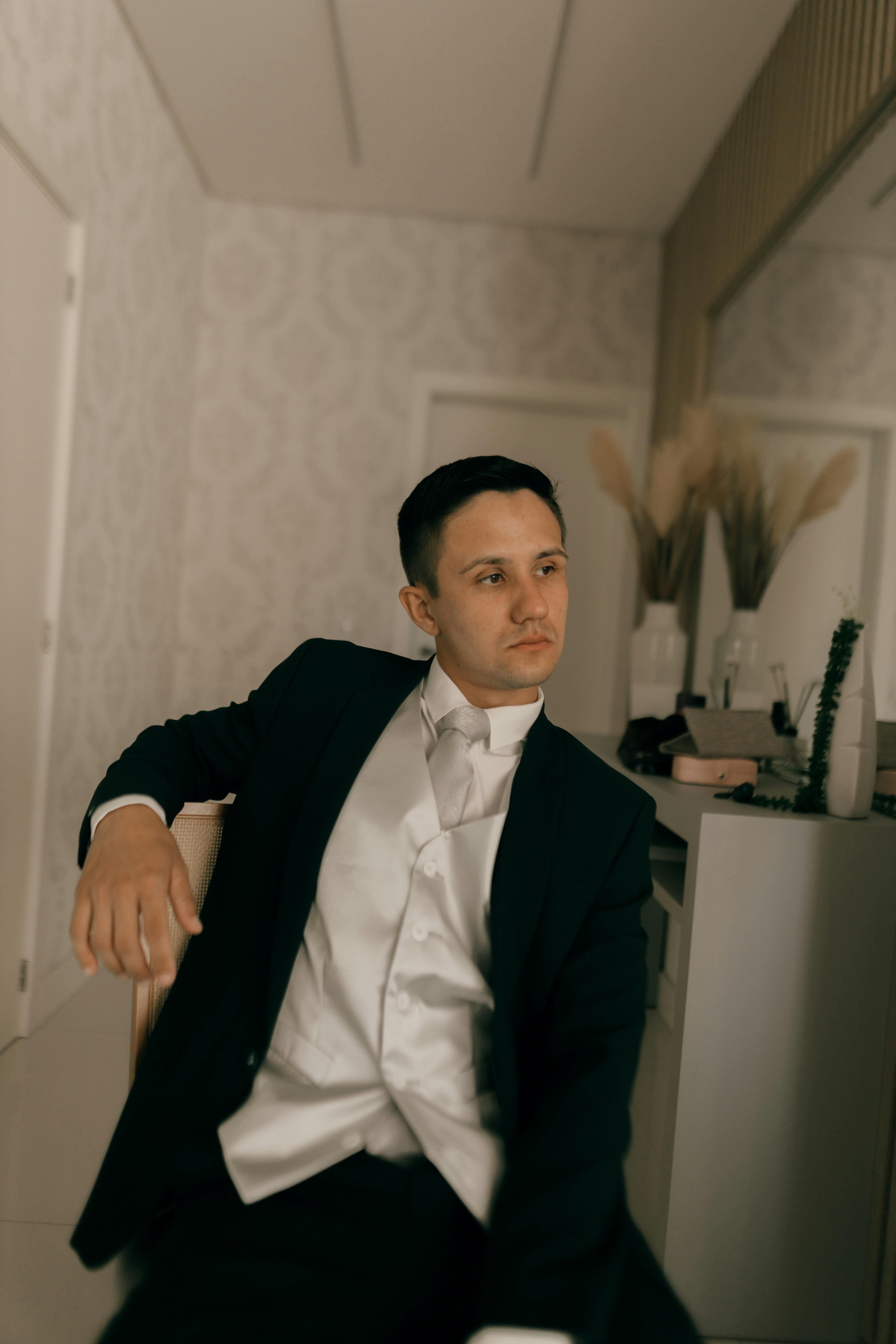 Gratis Un hombre sofisticado con un traje elegante se sienta relajado en un elegante ambiente interior. Foto de stock