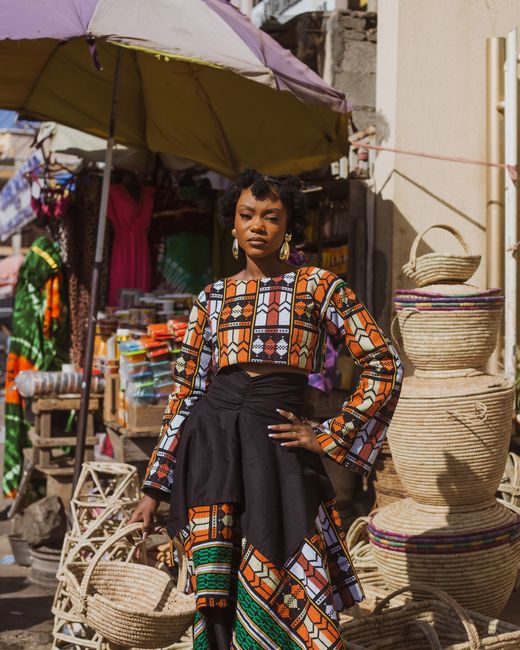 Stylish woman poses in vibrant traditional attire at an outdoor market.