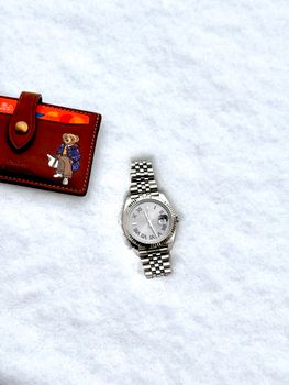 Silver watch and leather wallet with bear illustration on white snowy background, high contrast.