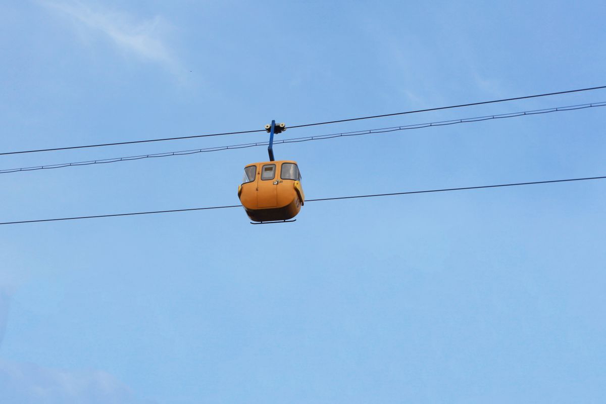 A solitary orange cable car suspended in motion with a clear blue sky backdrop.