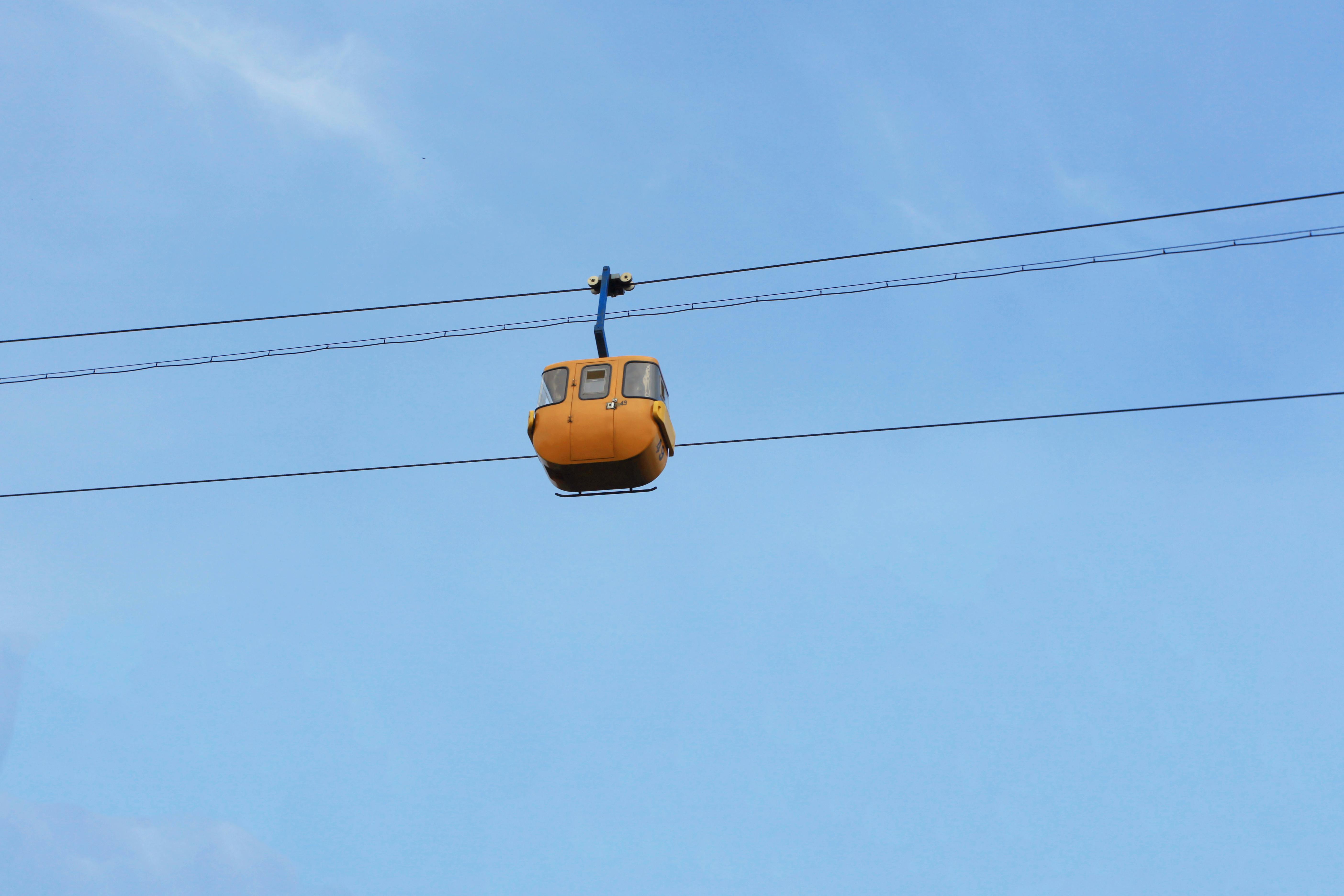 Gratis Un teleférico naranja solitario suspendido en movimiento con un cielo azul claro de fondo. Foto de stock
