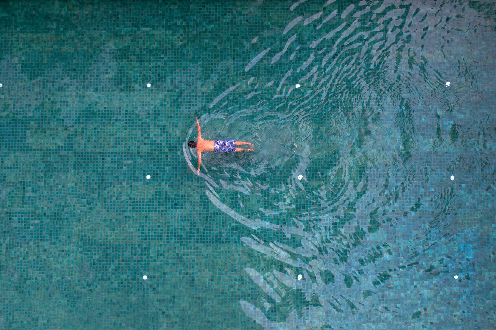 Swimmer floating in a turquoise pool seen from above