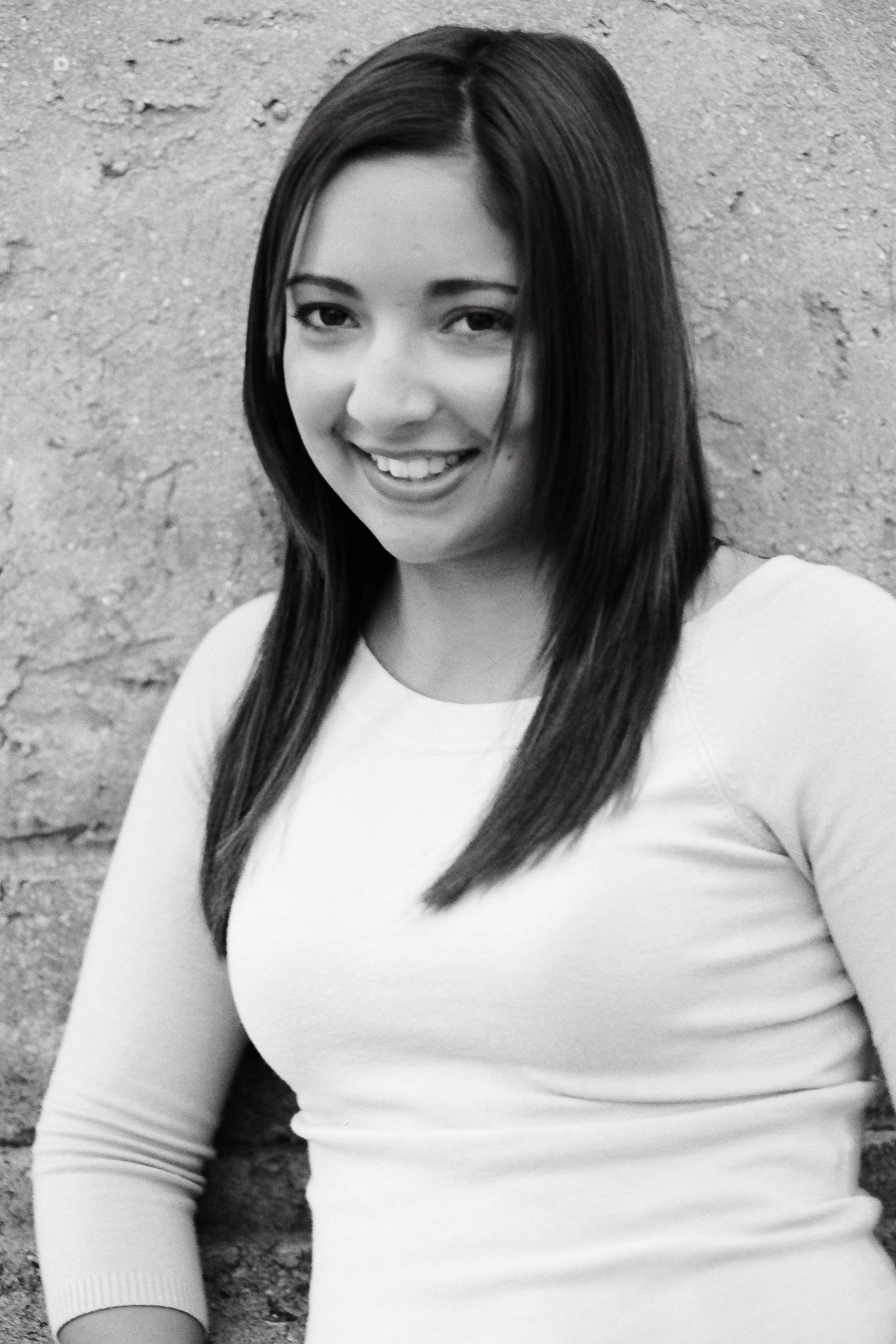 Black and white photo of a smiling woman leaning against a stone wall.