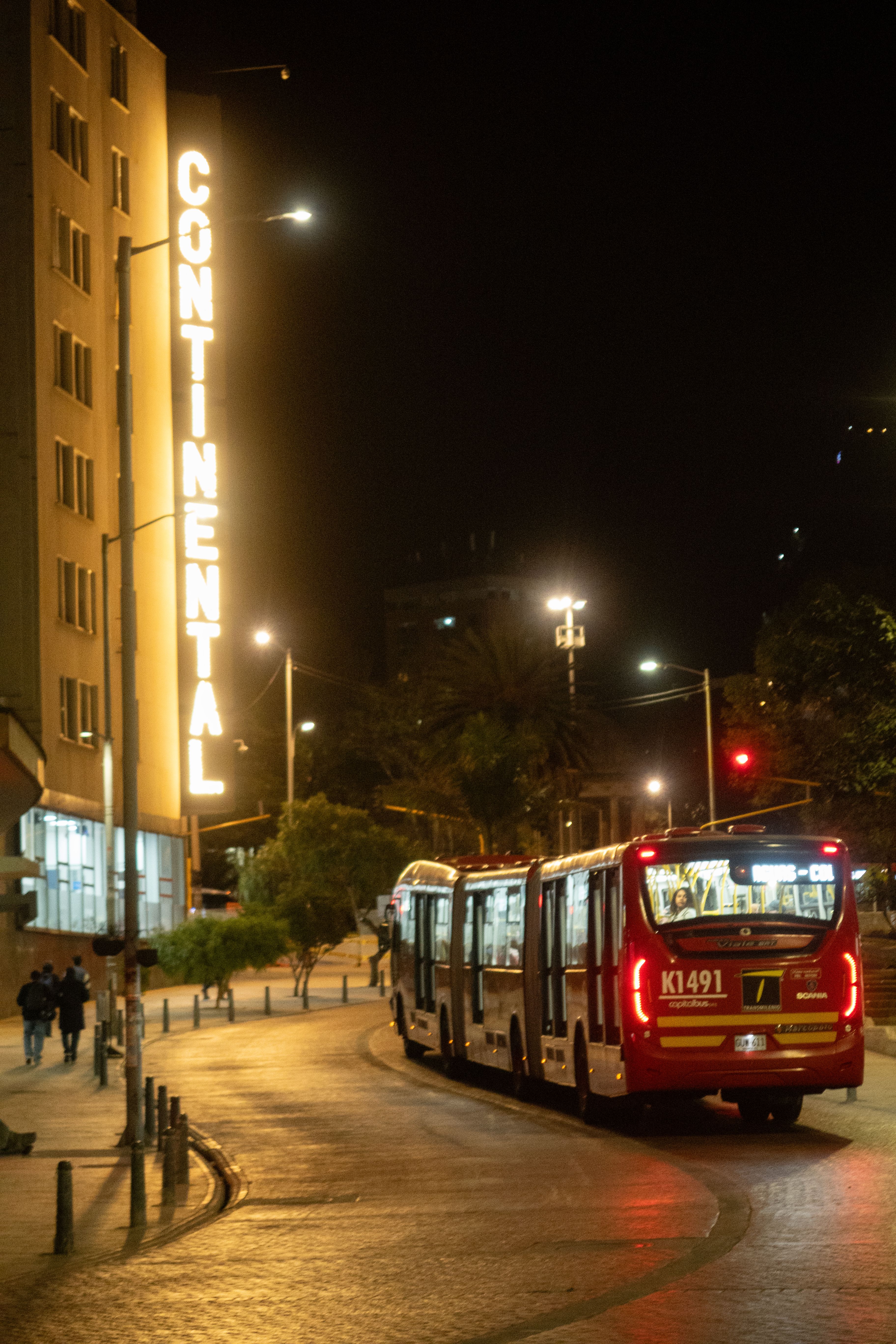TransMilenio bus navigating Bogotá streets at night with Continental hotel sign.