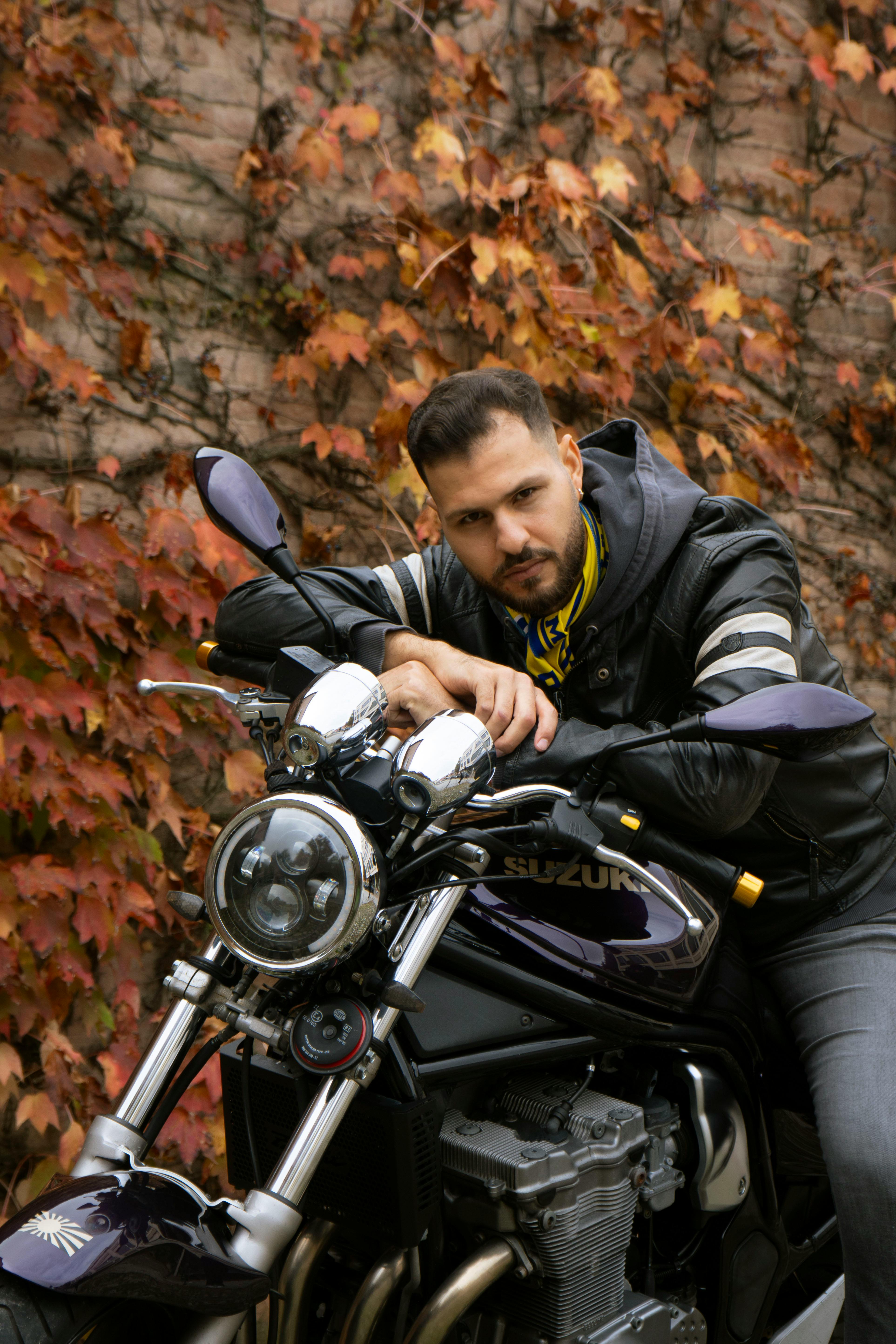 Man in black leather jacket on motorcycle against a backdrop of autumn leaves.