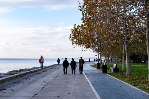 Free An autumn scene with people walking along the waterfront path, surrounded by trees. Stock Photo