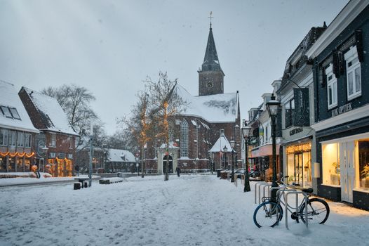 Charming snow-covered street with a historic church and festive lights.