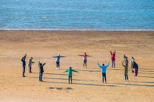 A group of people exercising on a sandy beach with the sea in the background, using green hoops.