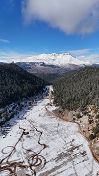 Breathtaking aerial view of a snowy mountain landscape in Antalya, Türkiye, with winding paths and a crisp blue sky.
