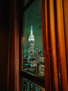 Night view of the illuminated Empire State Building seen through a window in NYC.