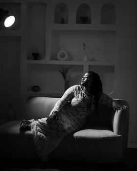 Black and white portrait of a woman in a lace dress on a sofa, dramatic lighting.