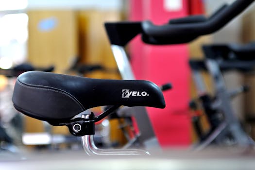 Detailed focus on a black bicycle saddle with gym equipment in the background.