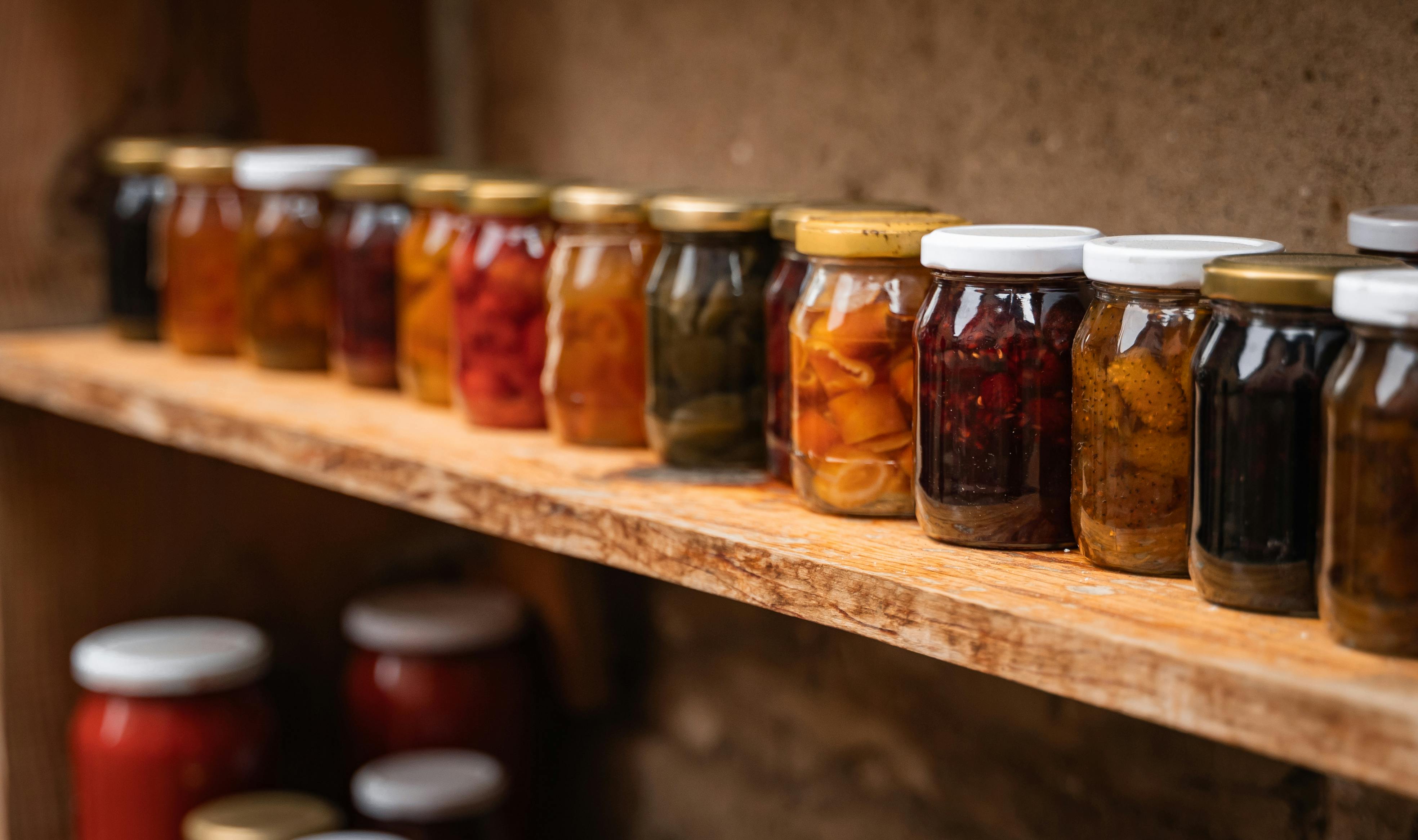 Homemade preserves in mason jars neatly arranged on a rustic wooden shelf.