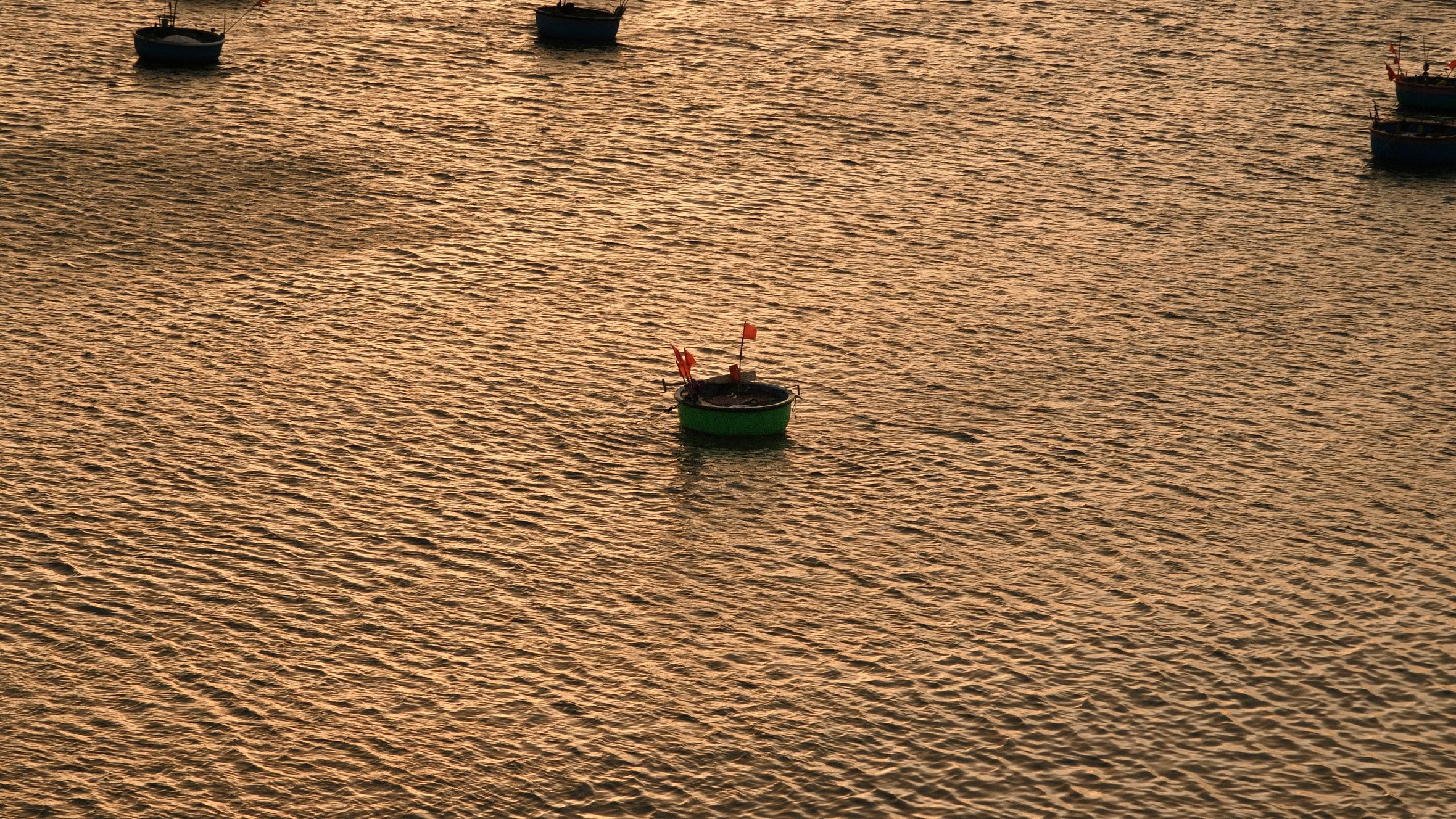Serene view of basket boats floating in the golden sunset light on rippling water in Phan Thiết, Vietnam.