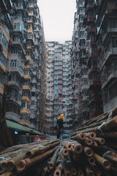 A construction worker handling bamboo scaffolding amidst high-rise buildings in Hong Kong.