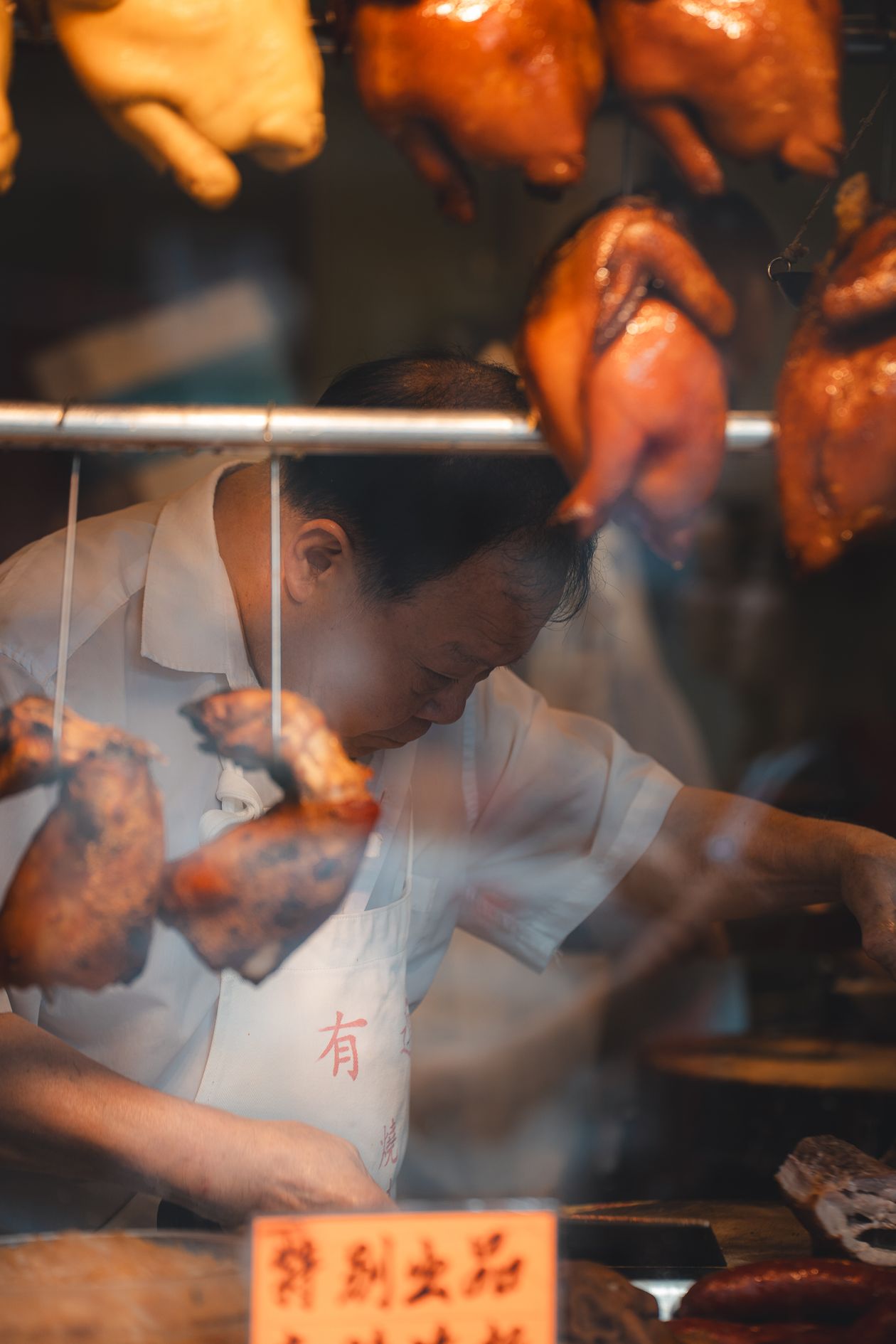 A man preparing roasted duck at a Hong Kong street food stall, hanging poultry visible behind him